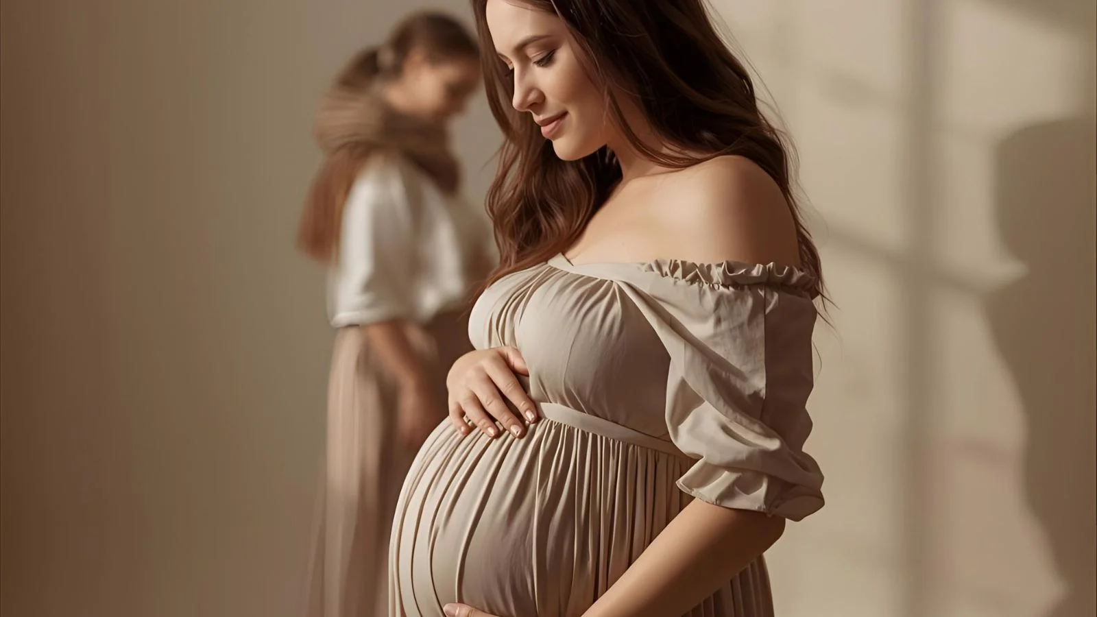 Pregnant woman in a soft-lit studio cradling her baby bump during a maternity photoshoot.
